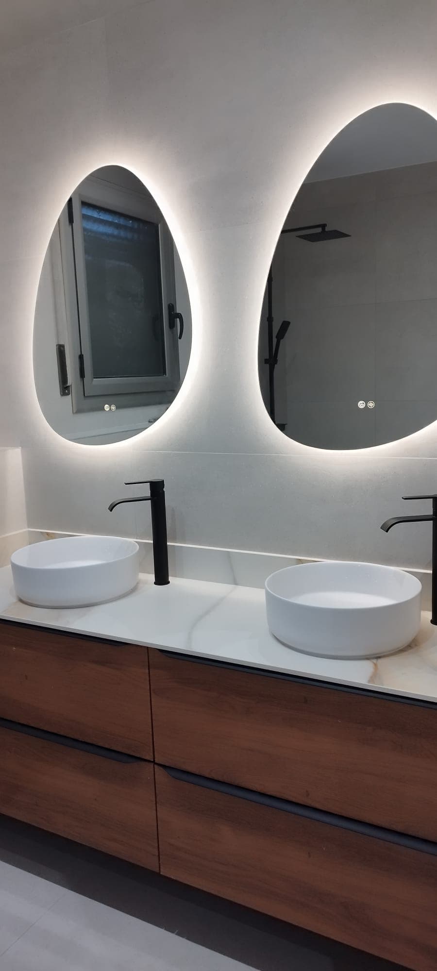 Doble lavabo con espejos ovalados retroiluminados sobre mueble de nogal