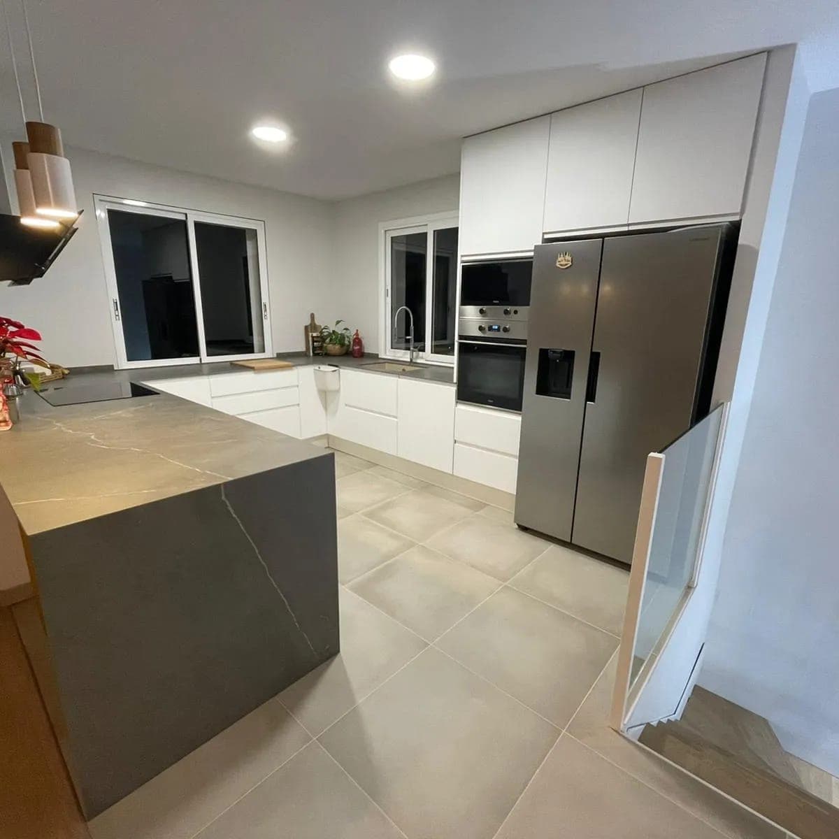 Cocina con isla de piedra, armarios blancos y nevera americana